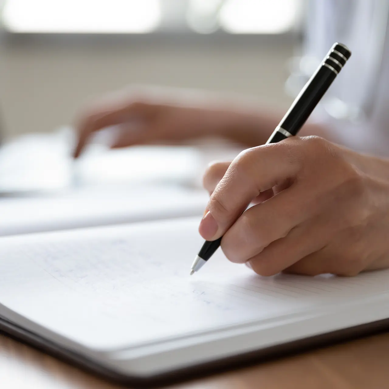woman writing in journal while using laptop